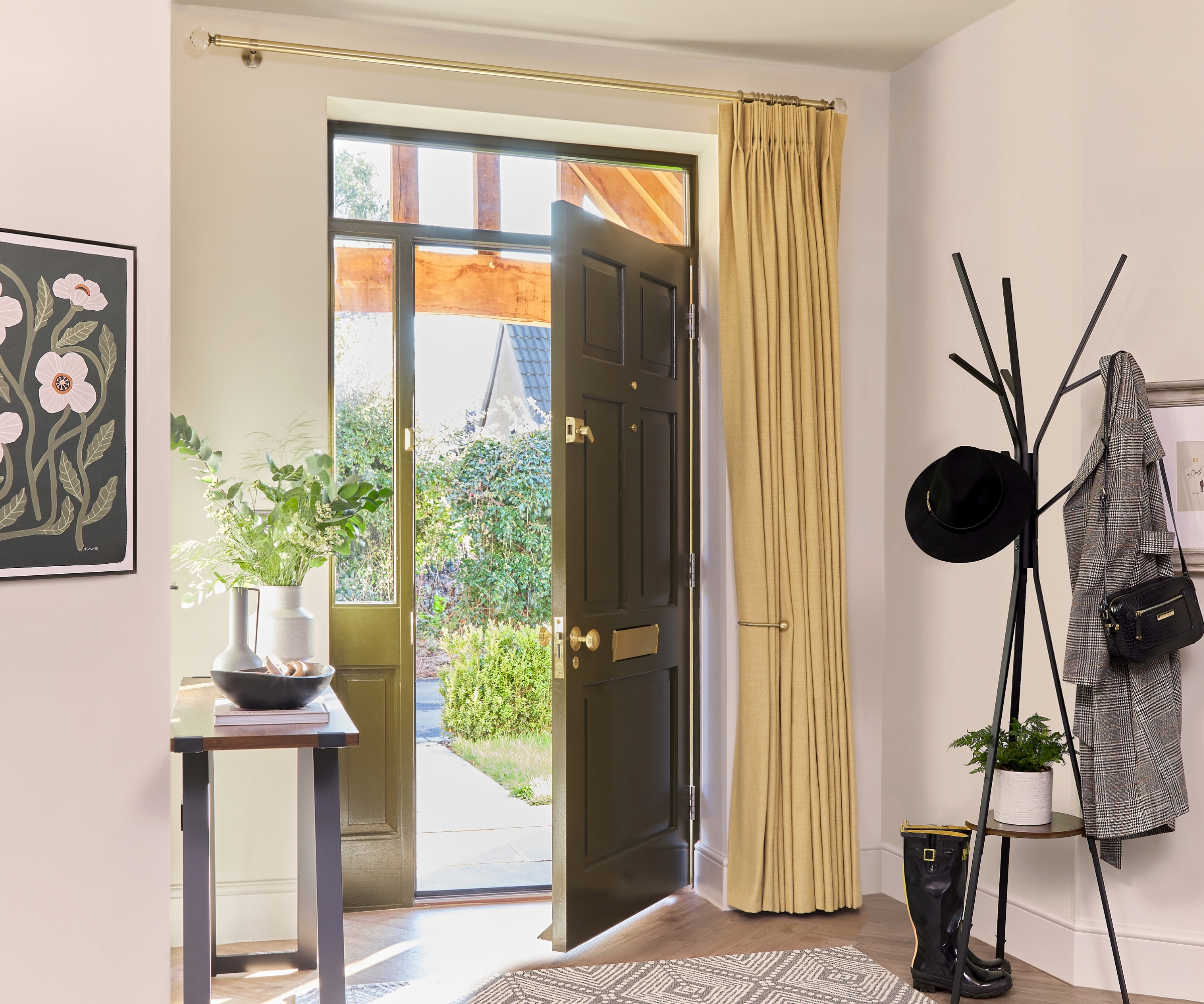 Open black front door with mustard curtain beside, coat stand with hat and wellies, console table with vase.