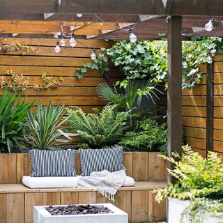 Pergola and wooden seating area and fire pit with surrounding potted plants