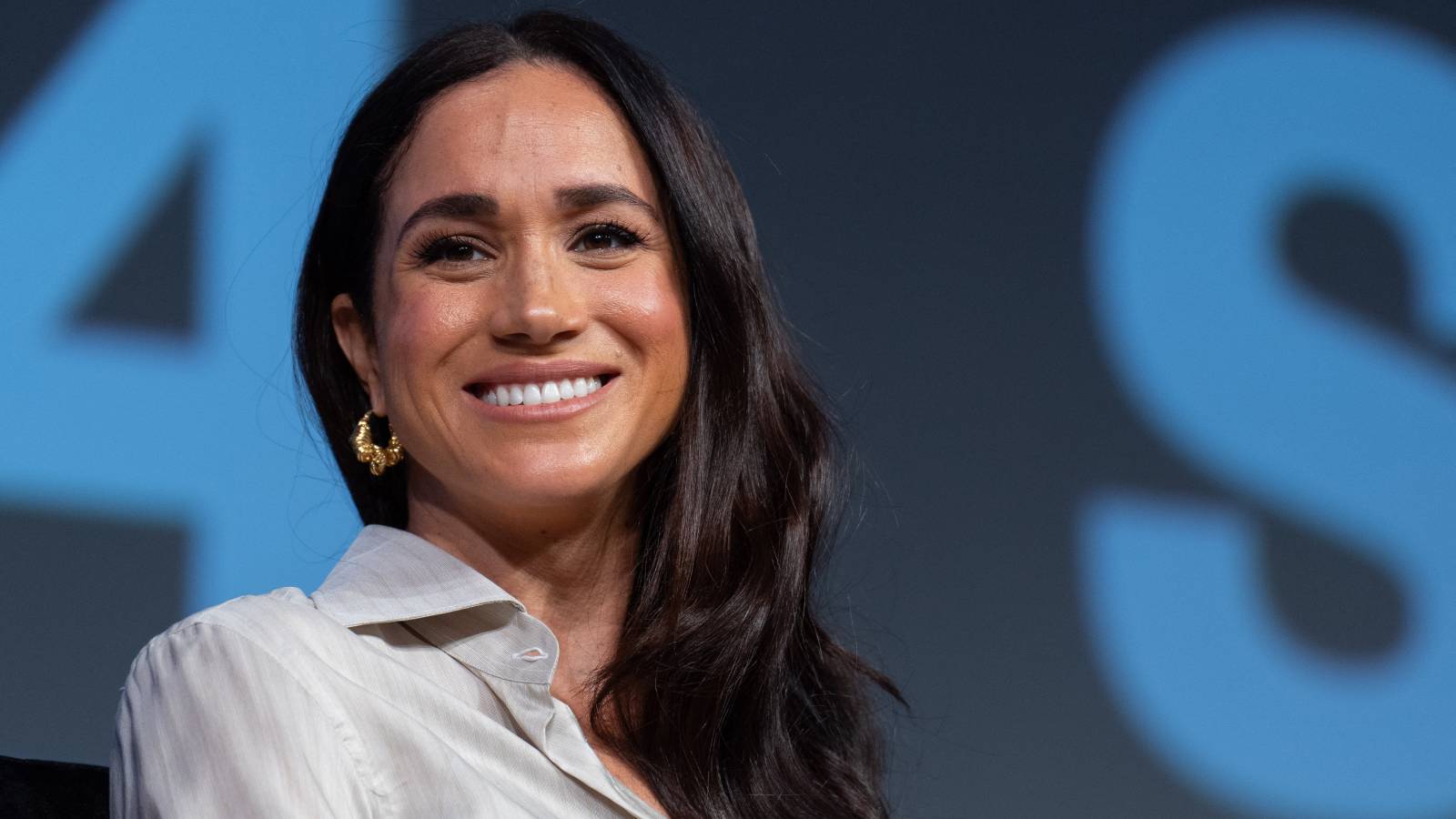 Meghan Markle smiles in front of a blue background