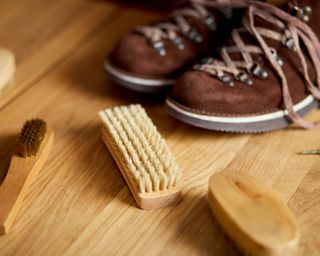 A pair of brown suede shoes with a brown bristle suede brush on a wooden surface