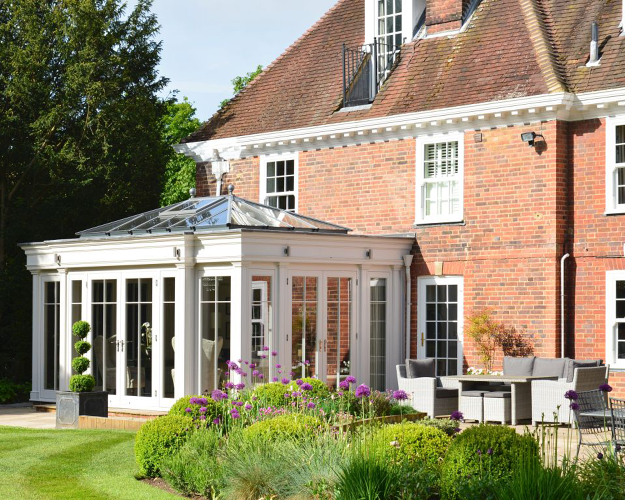 White orangery by David Salisbury with grey rattan furniture set and manicured lawn