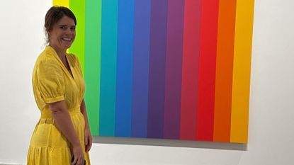 Princess Eugenie wearing a yellow dress standing in front of a rainbow painting