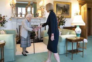 Queen Elizabeth standing in front of a fireplace and green sofas and shaking hands with Liz Truss