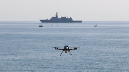 a flying naval drone with a ship in the background