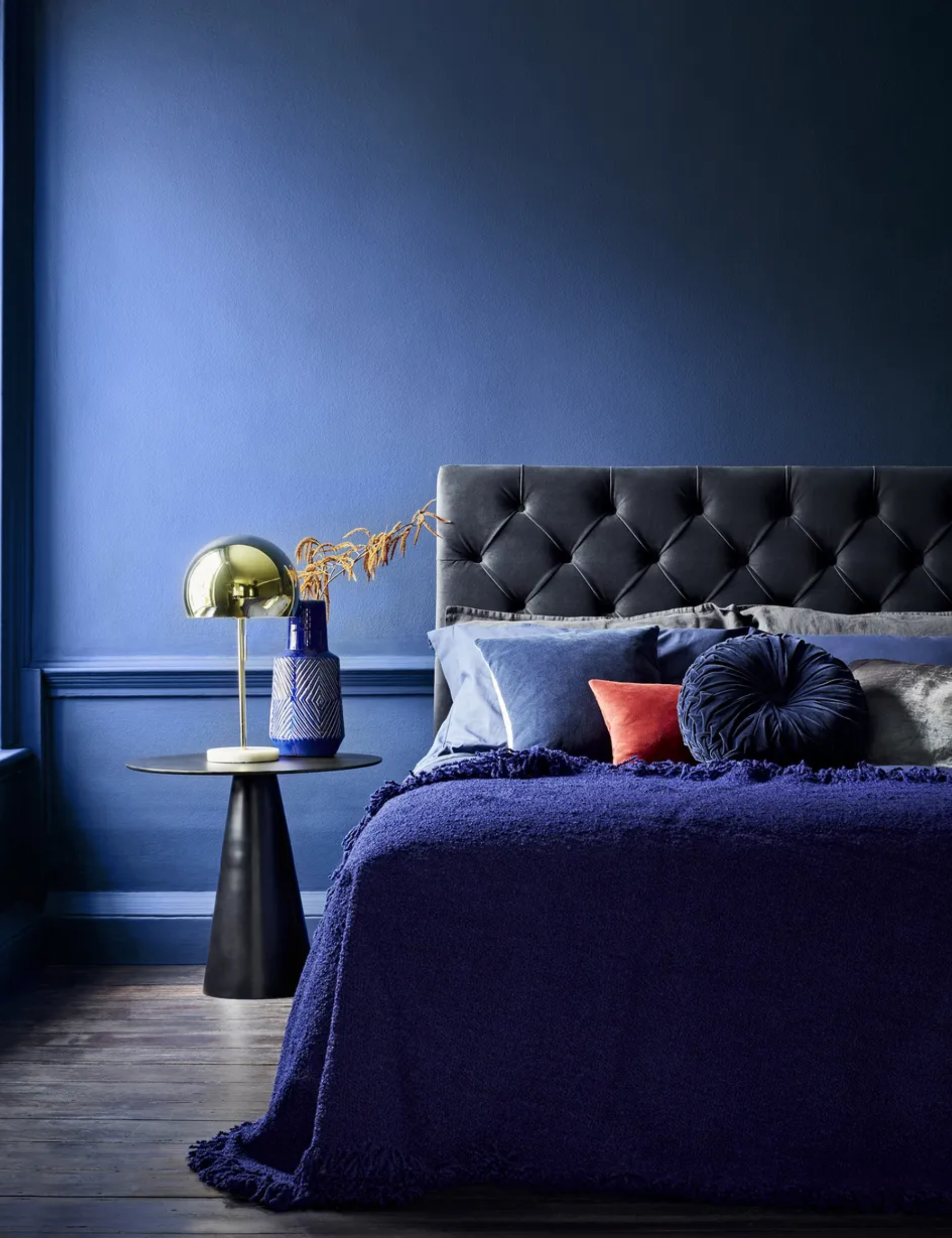 A bedroom with deep blue walls and a bed with blue velvet headboard