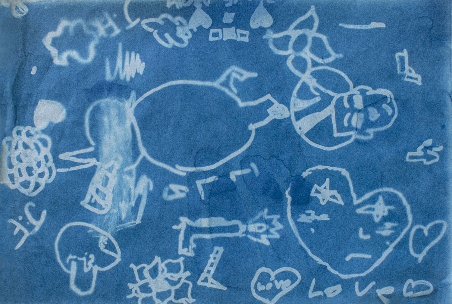 A bright blue cyanotype print displays white line drawings of various objects and shapes, including hearts, flowers, clouds, a gun, and an abstract figure.