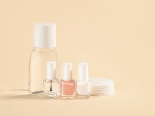 Nail varnish remover, white, pale pink and clear nail polish, cotton pads on a powdery colour background.