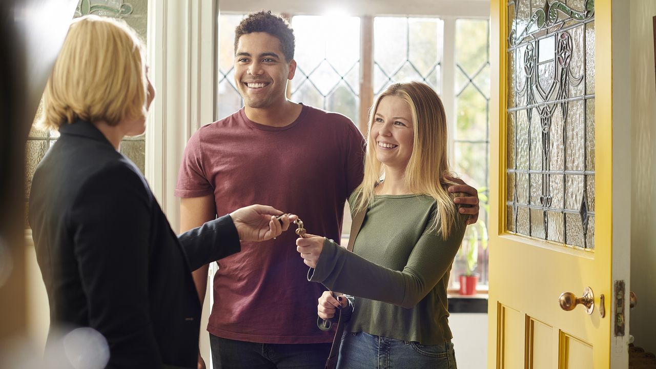 A landlord hands the keys over to her new tenants, a young couple.