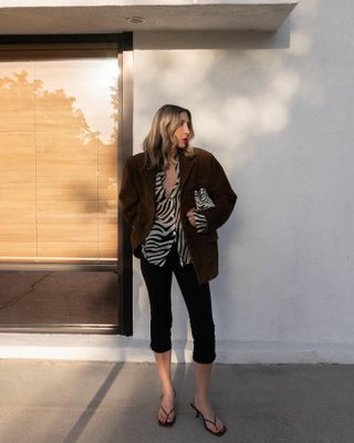 Los Angeles
based influencer Angela Fink poses on a sidewalk wearing a brown blazer, sheer zebra-print button-down shirt, zebra-print bag, capri pants and flip-flop sandals