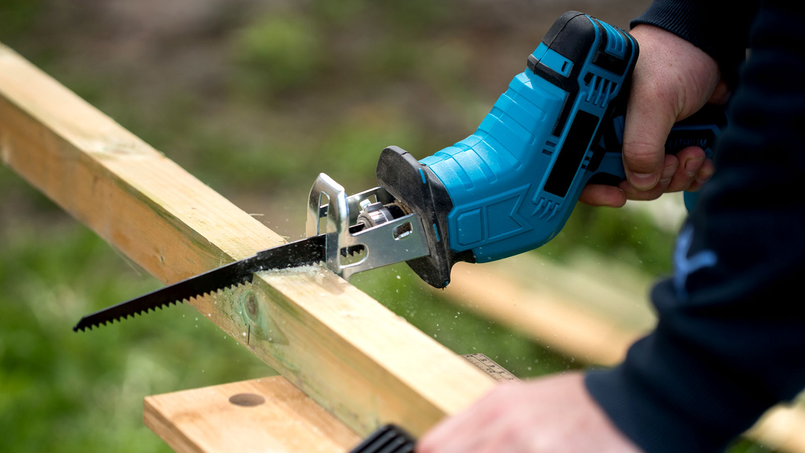 Person holding blue reciprocating saw sawing through wooden post outside