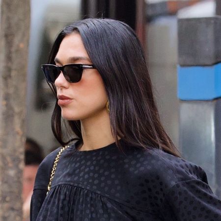 Dua Lipa wearing a black top, black jeans, and black sunglasses