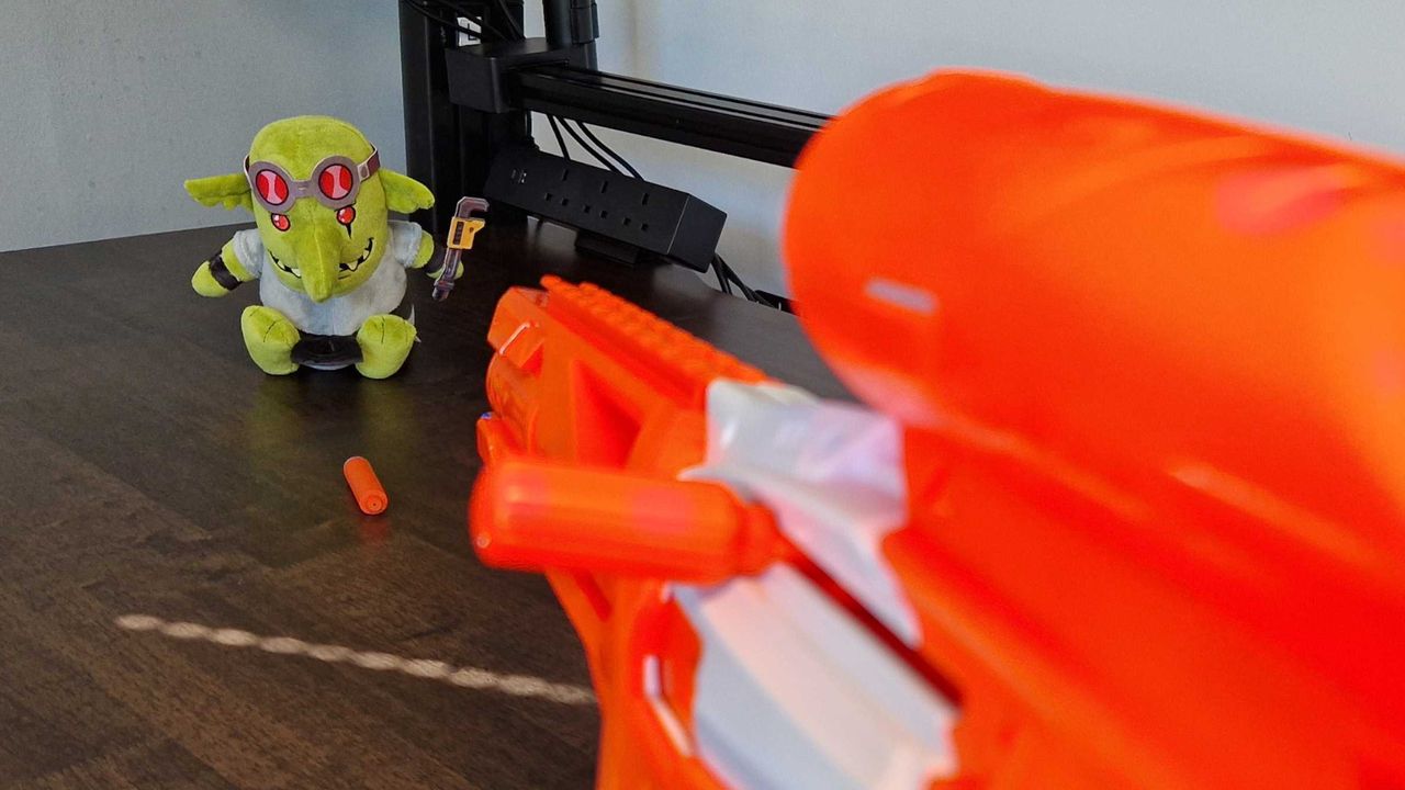 Nerf N-Series Pinpoint blaster aiming at a plush toy sitting on a wooden table