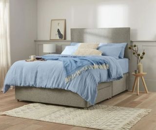 Blue and white bedding on a gray bed frame against a white wall.