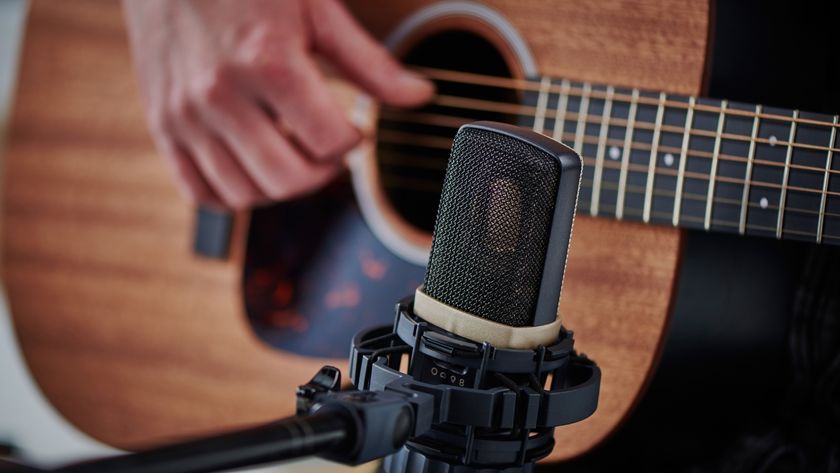 An AKG condenser microphone on a shock mount in front of a man playing acoustic guitar