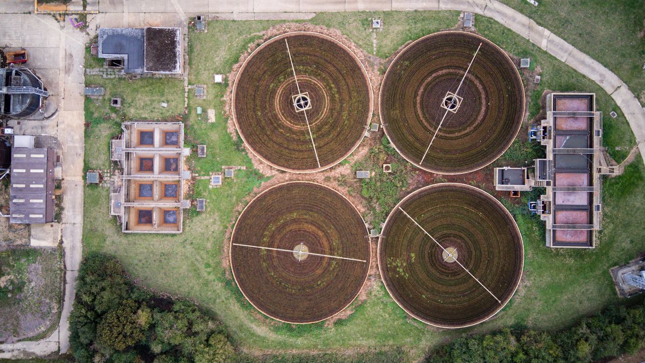 Aerial view above agricultural implements, which form four circles, each with bisecting lines at various angles. grass surrounds, as well as rectangular constructions.