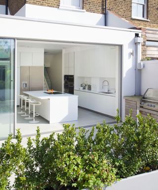 white kitchen with white tiles next to huge glass door leading to the white patio with white walls