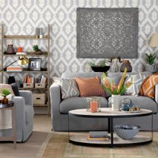 Modern living room with grey geometric wallpaper, grey sofa, assorted coloured geometric cushions. 