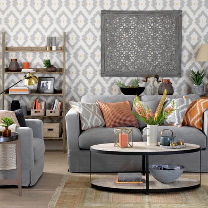 Modern living room with grey geometric wallpaper, grey sofa, assorted coloured geometric cushions. 