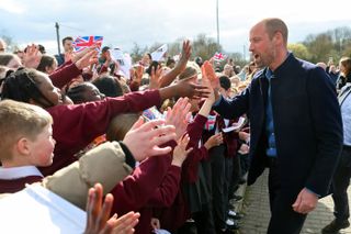 Prince William giving high fives to a large group of school children waving flags during a March 2025 soccer event