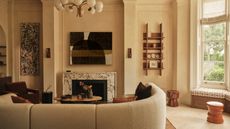 Living room with warm white limewash walls, cream curved corner sofa, rust armchair, rust rug, stacked wood coffee table and globe chandelier
