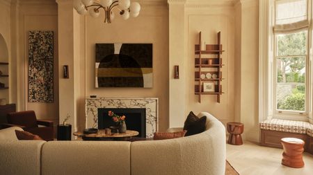 Living room with warm white limewash walls, cream curved corner sofa, rust armchair, rust rug, stacked wood coffee table and globe chandelier