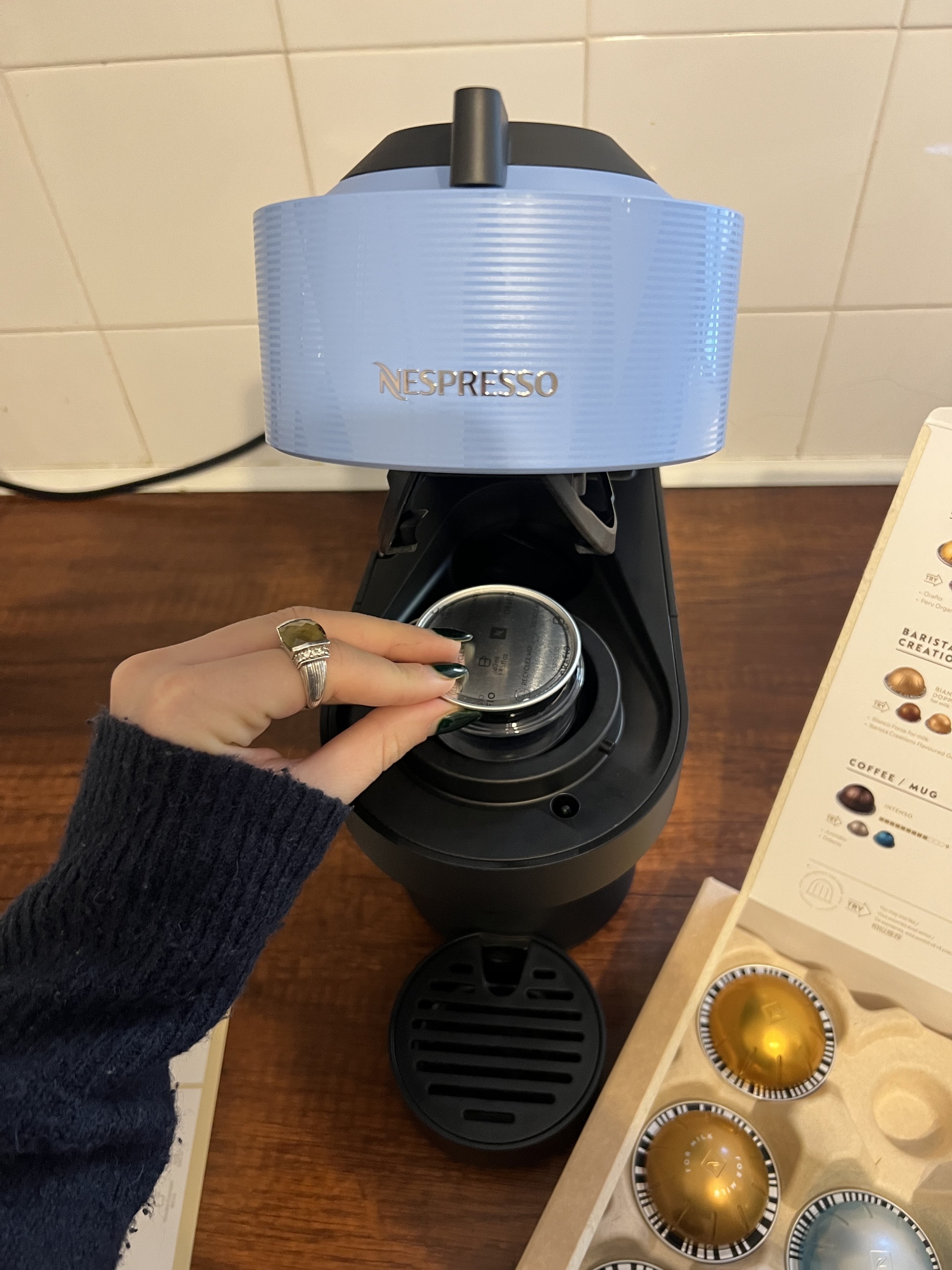 Image of a hand putting a Vertuo pod into Nespresso's Vertuo Pop machine in black and blue.