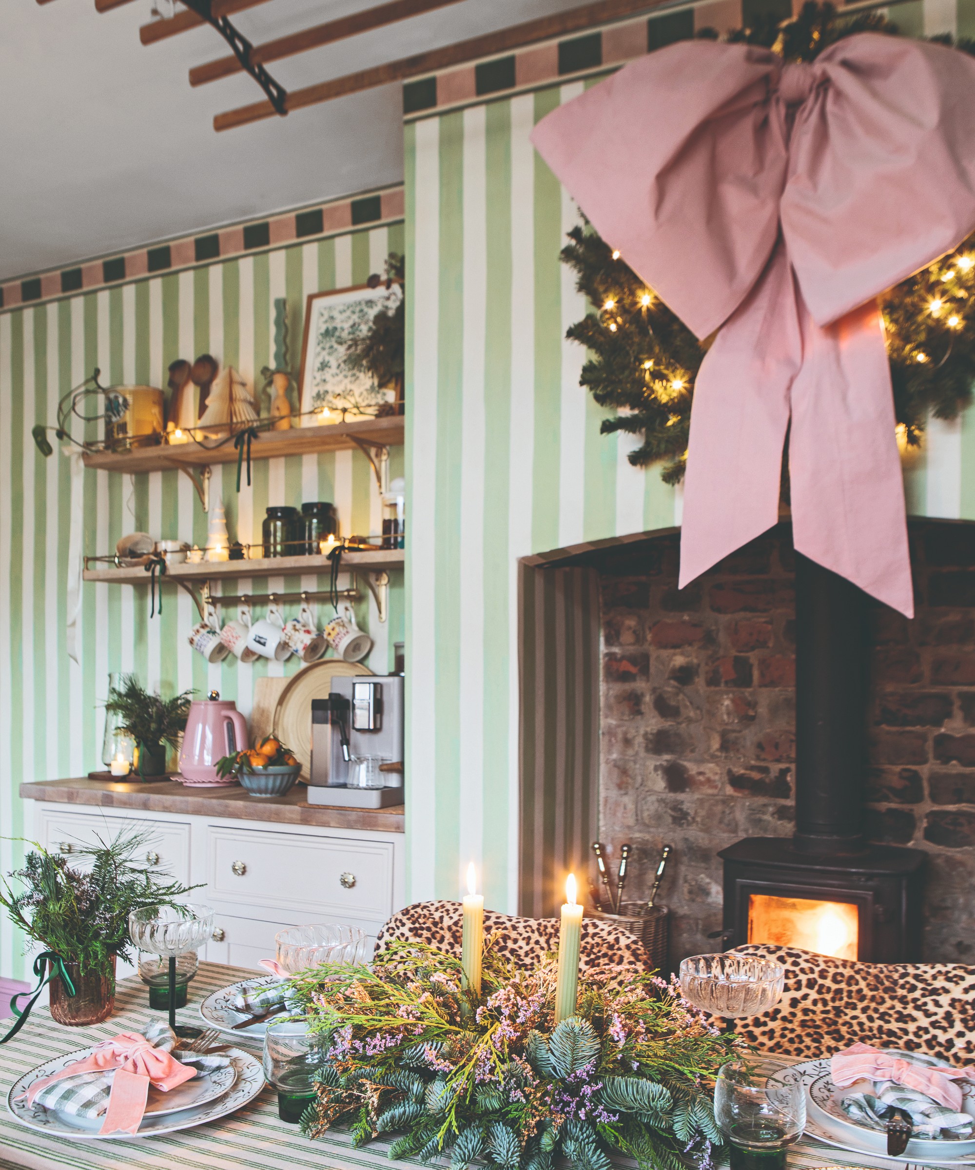 A kitchen with striped walls decorated for Christmas with a wreath with a large pink bow