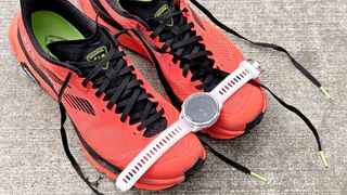 Close-up of the Rossignol Vezor trail running shoes in bright red/orange next to the Garmin Forerunner 570 smartwatch