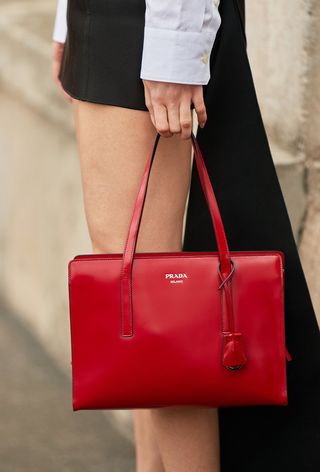 a close up photo of a woman holding a red prada bag