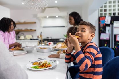 Boy happily eating from dinner plate in the kitchen with family