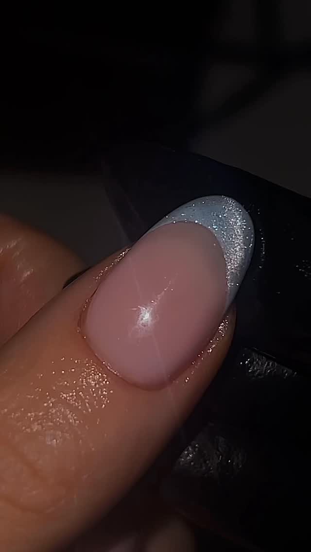 A very close-up photo of nail painted with a sheer pink base and a silver glittery French tip by @bambinailss