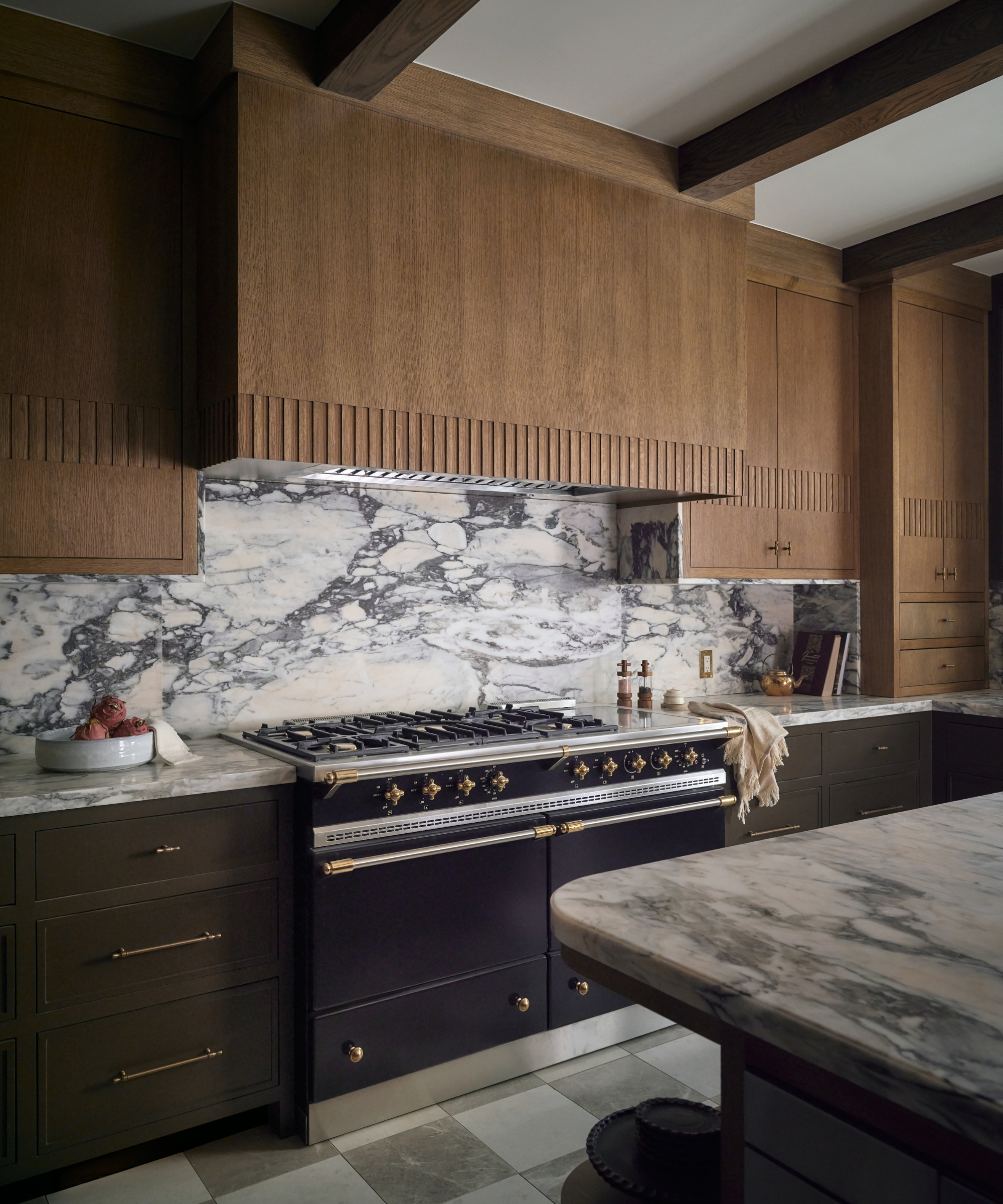 A traditional kitchen with white oak cabinets featuring a fluted detail around the middle and at the base of the range hood
