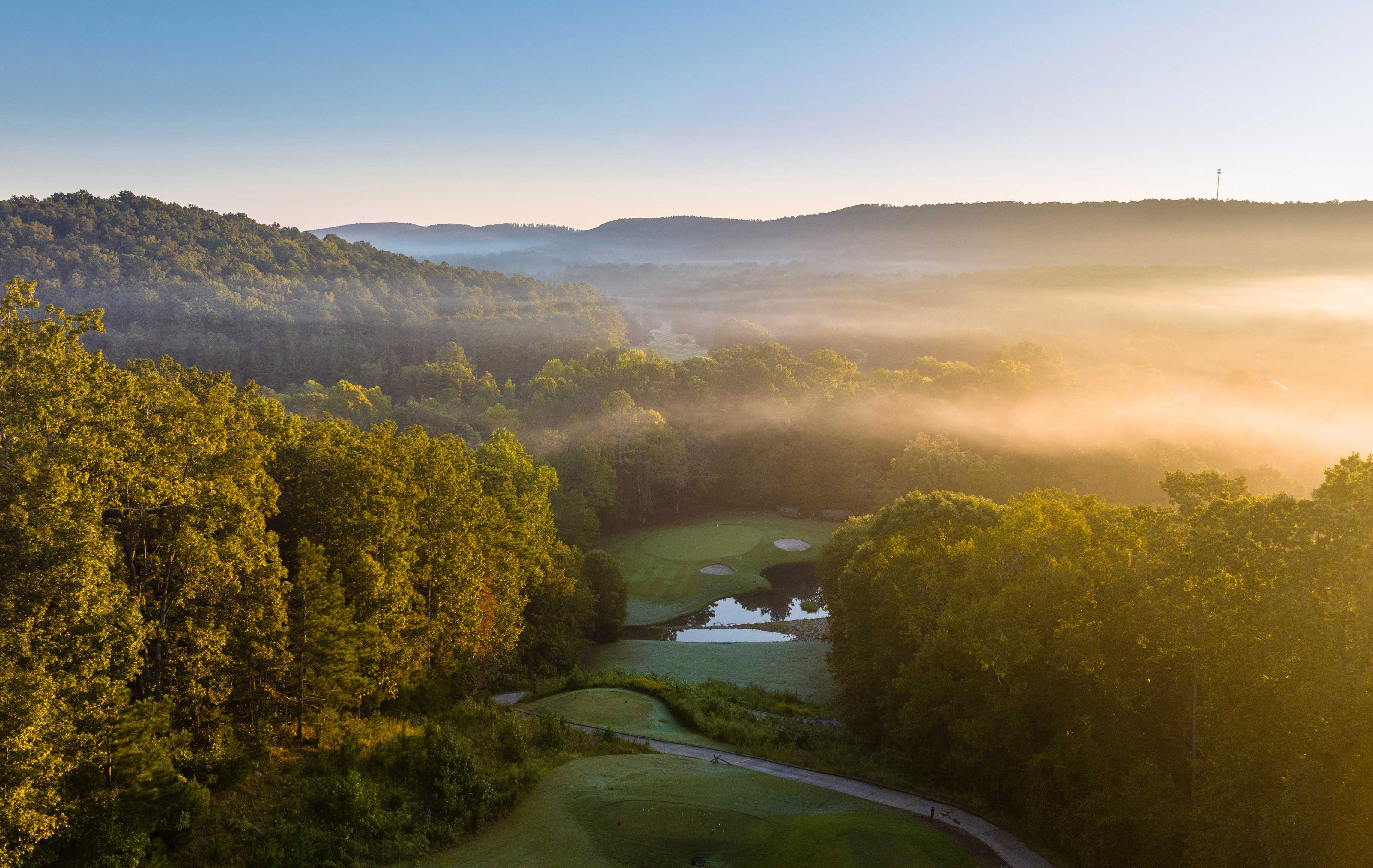 An aerial view of the Barnsley Resort golf course with forests and mist in the background.