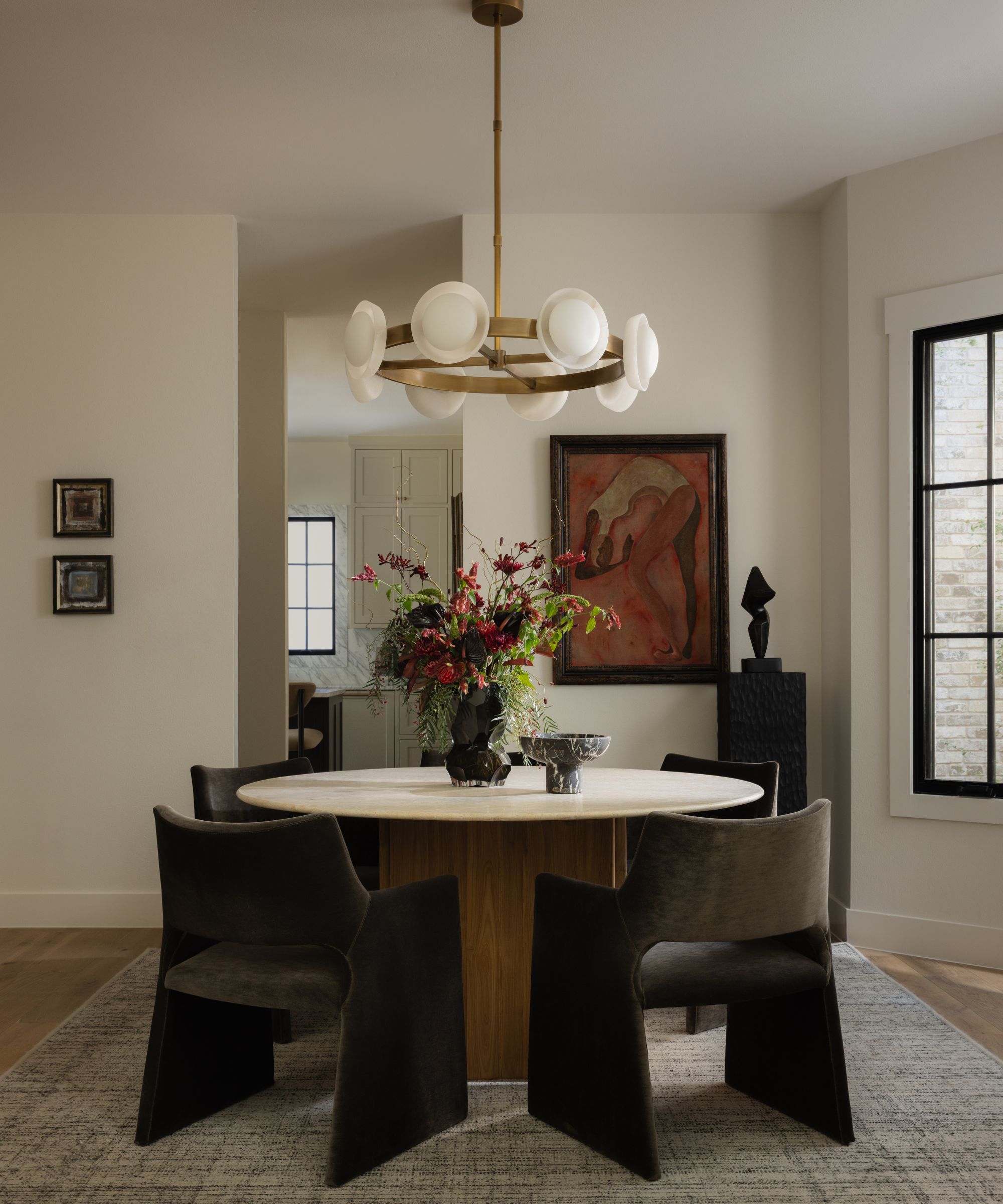 a neutral dining room with angled walls with a rounded table, velvet green chairs and a statement brass pendant