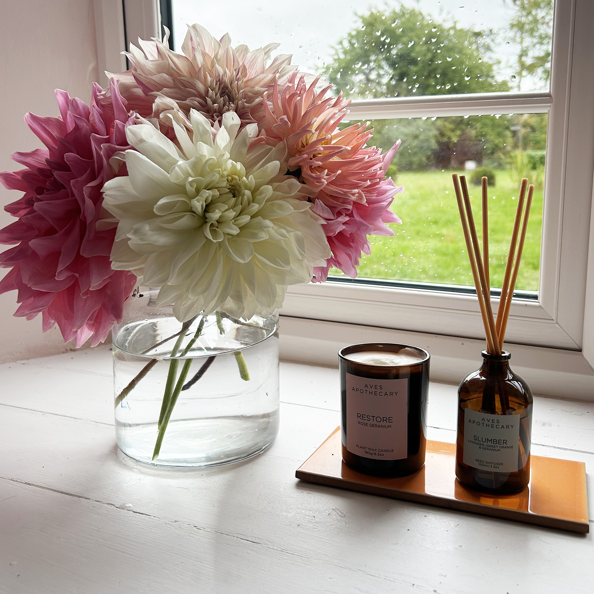 candle and reed diffuser on a window ledge with dahlias