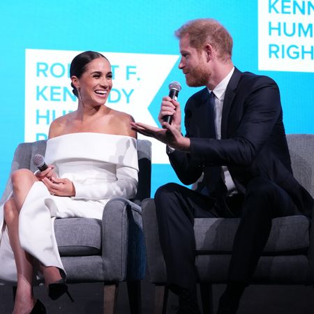 Prince Harry and Meghan Markle look at each other while speaking into microphones on a stage