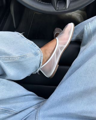 British fashion influencer Marianne Smyth poses in her car wearing light-wash jeans and white mesh flats.