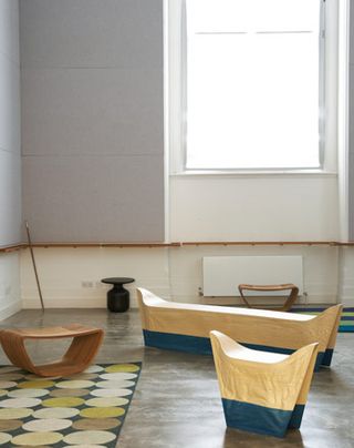 Bench-like objects on display in a room with tall windows, concrete floor and grey walls