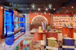 A vintage-inspired, contemporary retail space features exposed bricks and orange plastered walls, and houses a colorful selection of stationery products, including notebooks, cards, and pens.