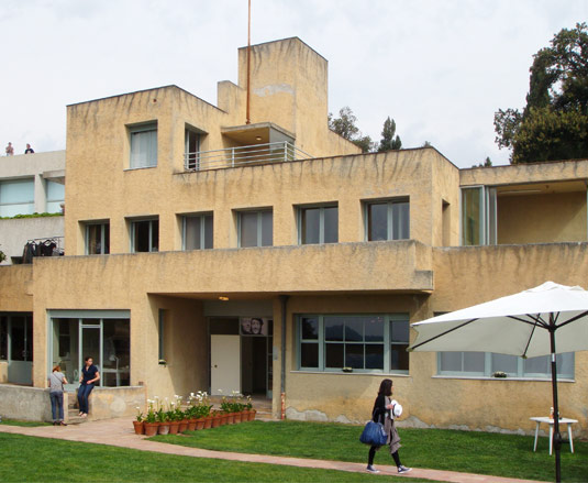 Outside Villa Noailles. A faded yellow three storey building with a green lawn in front of it.