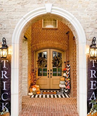 Halloween outdoor decor ideas on front porch with arched brick entry and black trick or treat slogan banners