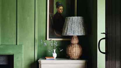 Rattan table light with fabric lamp shade on chest of drawers in front of green walls