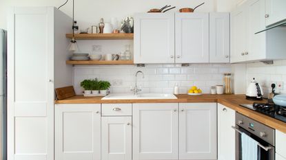 Kitchen with white walls, metro tiles and cabinetry with wooden countertops and floor