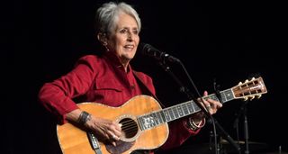 Folk legend Joan Baez wears a red shirt and plays her small-bodied Martin 0-40 acoustic guitar onstage in NYC