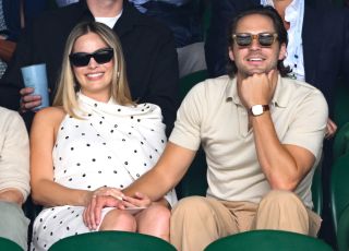 Margot Robbie and Tom Ackerley sitting hand in hand court-side of Centre Court on day twelve of the Wimbledon Tennis Championships at the All England Lawn Tennis and Croquet Club on July 12, 2024 in London, England. Margot Robbie is wearing a white dress with black polka dots.