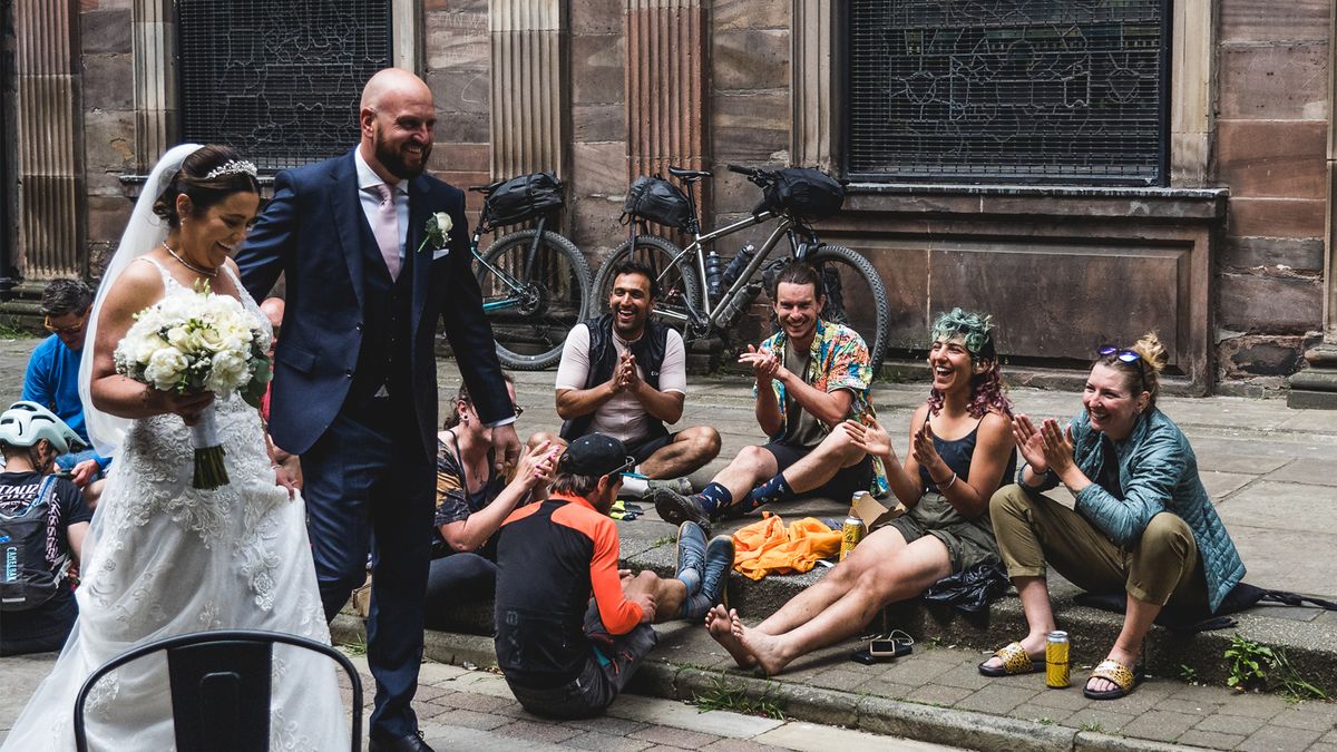 A bride and groom are clapped as they walk past a group of cyclists