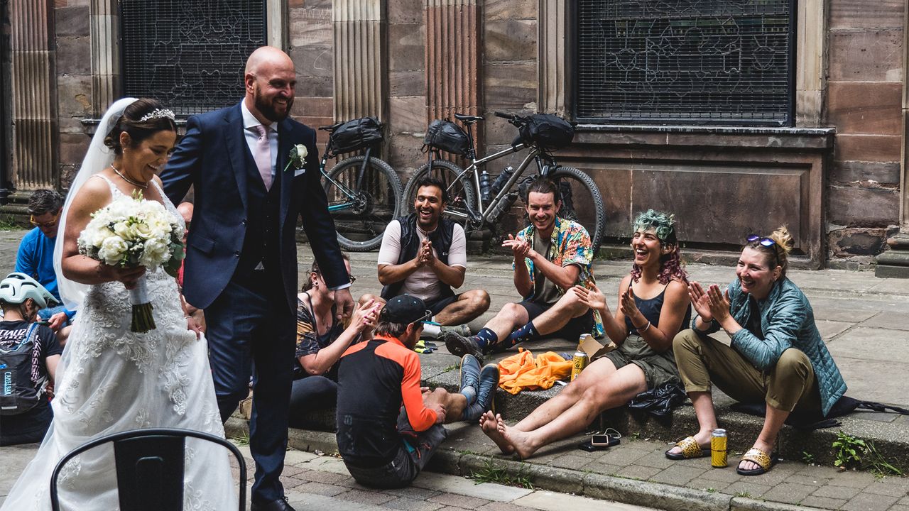 A bride and groom are clapped as they walk past a group of cyclists