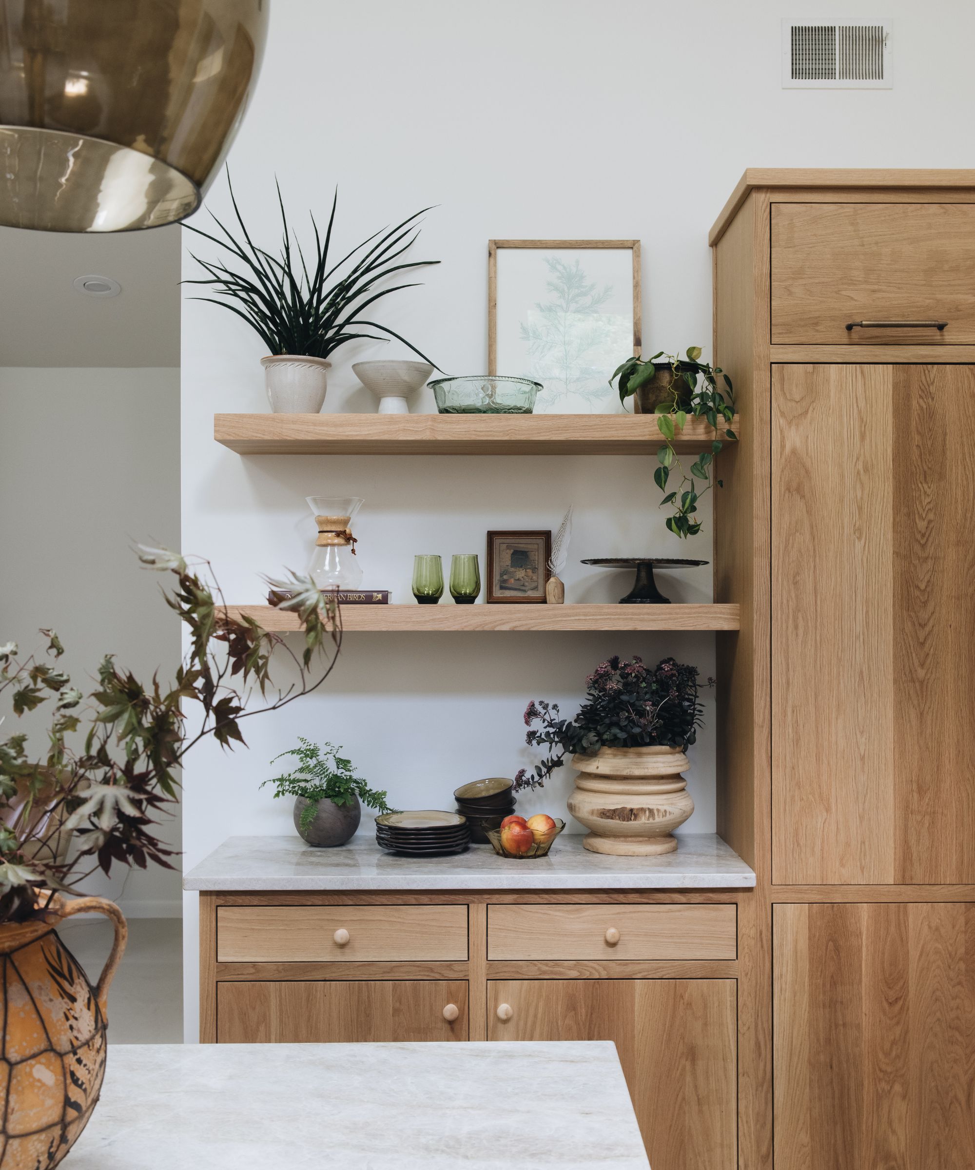 A kitchen with white walls, marble countertops, and wooden open shelving