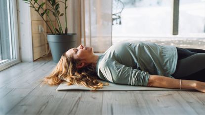 Woman lying down on yoga mat in studio at home, doing yoga for beginners