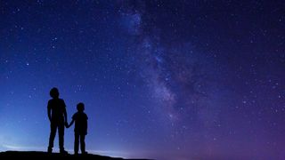 silhouettes of two children looking up at the night sky